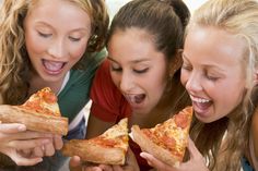 three girls are eating slices of pizza together