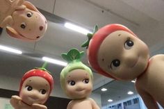 three toy figures are hanging from the ceiling in front of a store window, one is wearing a strawberries hat and another has a strawberry on it's head