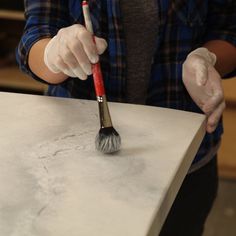 a person wearing gloves and holding a paintbrush on top of a white countertop