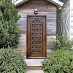 a wooden door sitting in the middle of a yard next to bushes and trees on either side of a house