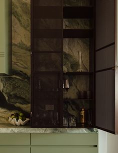 a kitchen with green cabinets and marble counter tops, along with an open cabinet door