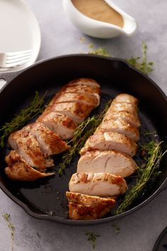 sliced pork in a skillet with herbs on the side