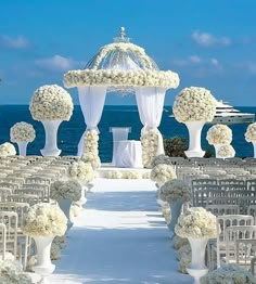 an outdoor wedding ceremony setup with white flowers and draping on the aisle, overlooking the ocean