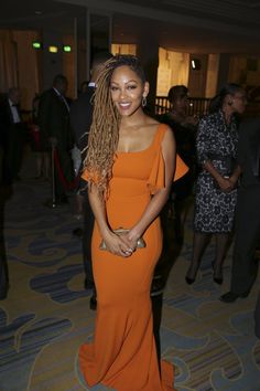 a woman in an orange dress standing next to other people at a party and posing for the camera