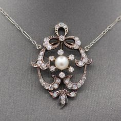 This is an absolutely exquisite necklace, beautifully crafted and replete with period details.  The necklace chain is crafted in 14k white gold while the pendant is crafted in silver topped 14k yellow gold.  The center natural pearl measures 5.5mm and is creamy white with lovely luster.  The rest of the design is encrusted with roundish chunky old cut diamonds.  The approximate carat weight is 0.74cttw.  The diamonds are bright white and lively, no eye visible inclusions.  The chain measures 16" and there pendant adds about another inch in width at the loops.  The pendant itself measures 1 3/8" in length and is just shy of 1" across in width.  The piece weighs 5.39g. Edwardian Necklace, Cabin Door, Diamond Bows, Diamond Heart Pendant Necklace, Bow Necklace, Art Deco Necklace, Clover Necklace, Silver Tops, Heart Pendant Diamond