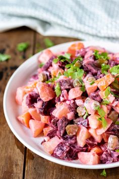 a white bowl filled with red cabbage salad on top of a wooden table next to a napkin