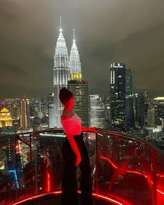 a woman standing on top of a tall building next to a cityscape at night