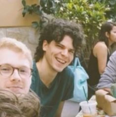 three people sitting at an outdoor table smiling