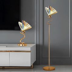 two gold colored lamps sitting on top of a white table next to a tv stand