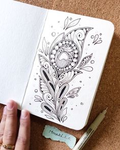 a person's hand is holding an open notebook with a peacock design on it