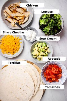 the ingredients to make chicken fajita laid out on a white counter top, including tortillas, lettuce, cheese and tomatoes