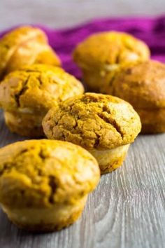 several muffins sitting on top of a wooden table next to a purple cloth