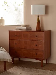 a wooden dresser sitting next to a bed in a room with pink walls and a lamp on top of it