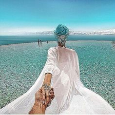 two people holding hands in front of the ocean with clear blue skies and water behind them