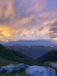 the sun is setting in the mountains with rocks and grass on the ground below it