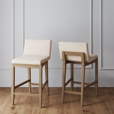 two wooden stools with white upholstered leather seats in front of a wall