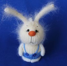 a white knitted bunny with blue overalls and an orange nose on a blue background