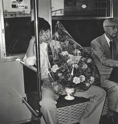 a man and woman sitting on a train next to each other with flowers in their lap