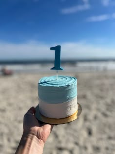 a hand holding a cake with the number one frosting on it at the beach