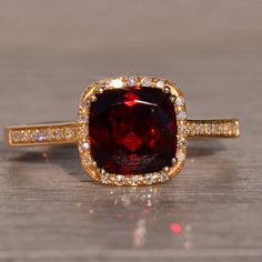 a ring with a large red stone surrounded by small white and yellow diamonds on a wooden surface