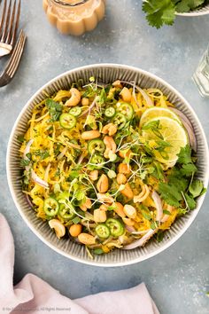 a white bowl filled with salad and garnished with cilantro, limes, cashews