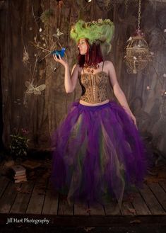 a woman wearing a purple and green dress holding a blue butterfly in her right hand