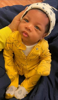 a baby sitting on top of a bed wearing a yellow shirt and white headband