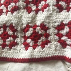 a red and white crocheted blanket laying on top of a bed