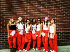 a group of women standing next to each other in front of a brick wall wearing orange pants