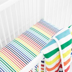 a crib bed with multicolored striped sheets and pillow cases on the side