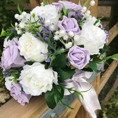 a bouquet of white and purple flowers sitting on top of a wooden bench with greenery