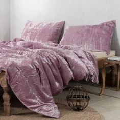 a bed with purple comforter and pillows on it in a room next to a table