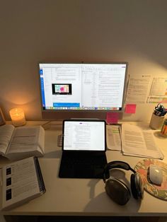 a laptop computer sitting on top of a desk next to headphones and an open book