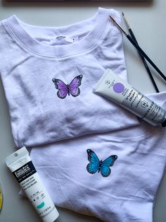 a t - shirt with butterflies painted on it next to some scissors and other items