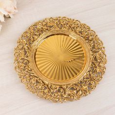 a gold plate with intricate designs on it and white flowers in the backgroud