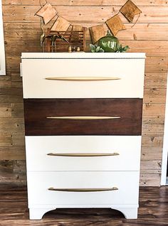 a white dresser with wooden drawers and gold handles on it's sides in front of a wood paneled wall