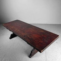 an old wooden bench sitting on top of a cement floor in front of a white wall