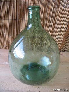 a green glass vase sitting on top of a wooden table next to a bamboo wall