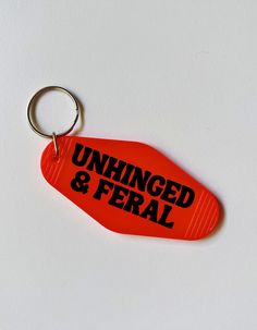 an orange keychain with the words unhinged and feral on it