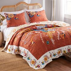 a bed with an orange and white comforter on top of it next to a wicker basket