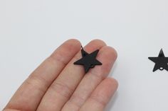 a hand holding a tiny black star shaped object next to another small, black one