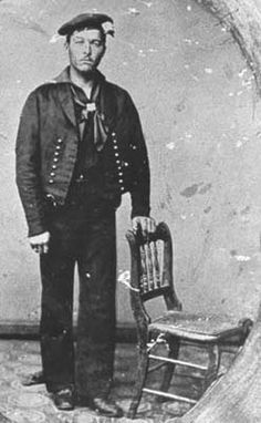 an old time photo of a man in uniform standing next to a chair and looking at the camera