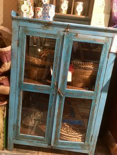 an old blue cabinet with baskets in it's glass doors and some other items on the shelf