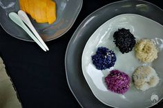 four different types of rice on a plate next to two bowls with silver spoons