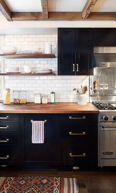 a kitchen with black cabinets and white subway backsplash, stainless steel stove top