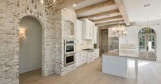 a large kitchen with white cabinets and an island in front of a brick wall that has a chandelier hanging from it's ceiling