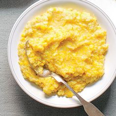 a white bowl filled with mashed potatoes on top of a gray tablecloth next to a spoon