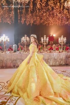 a woman in a yellow dress standing on a stage with candles and chandeliers