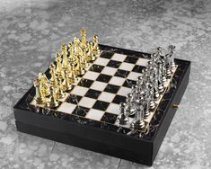 a black and white chess board with gold pieces on it's sides, sitting on a marble floor