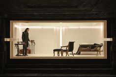 a man standing in front of a display case with chairs and furniture inside the window